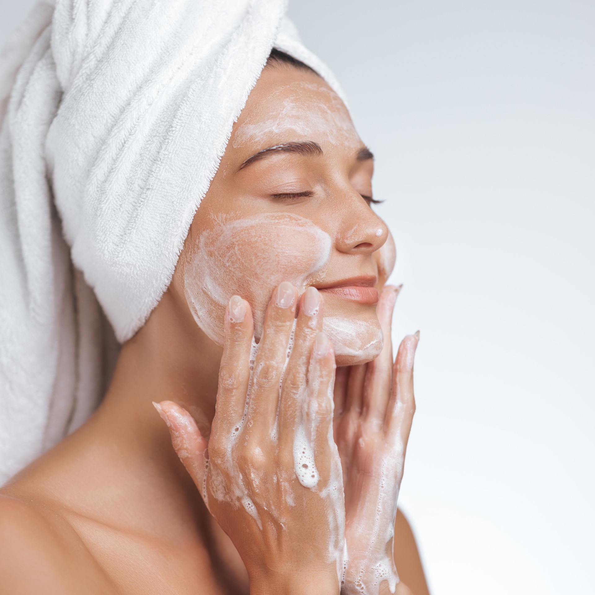 Woman Enjoying Skincare Routine with Foaming Cleanser and Towel Wrapped Head